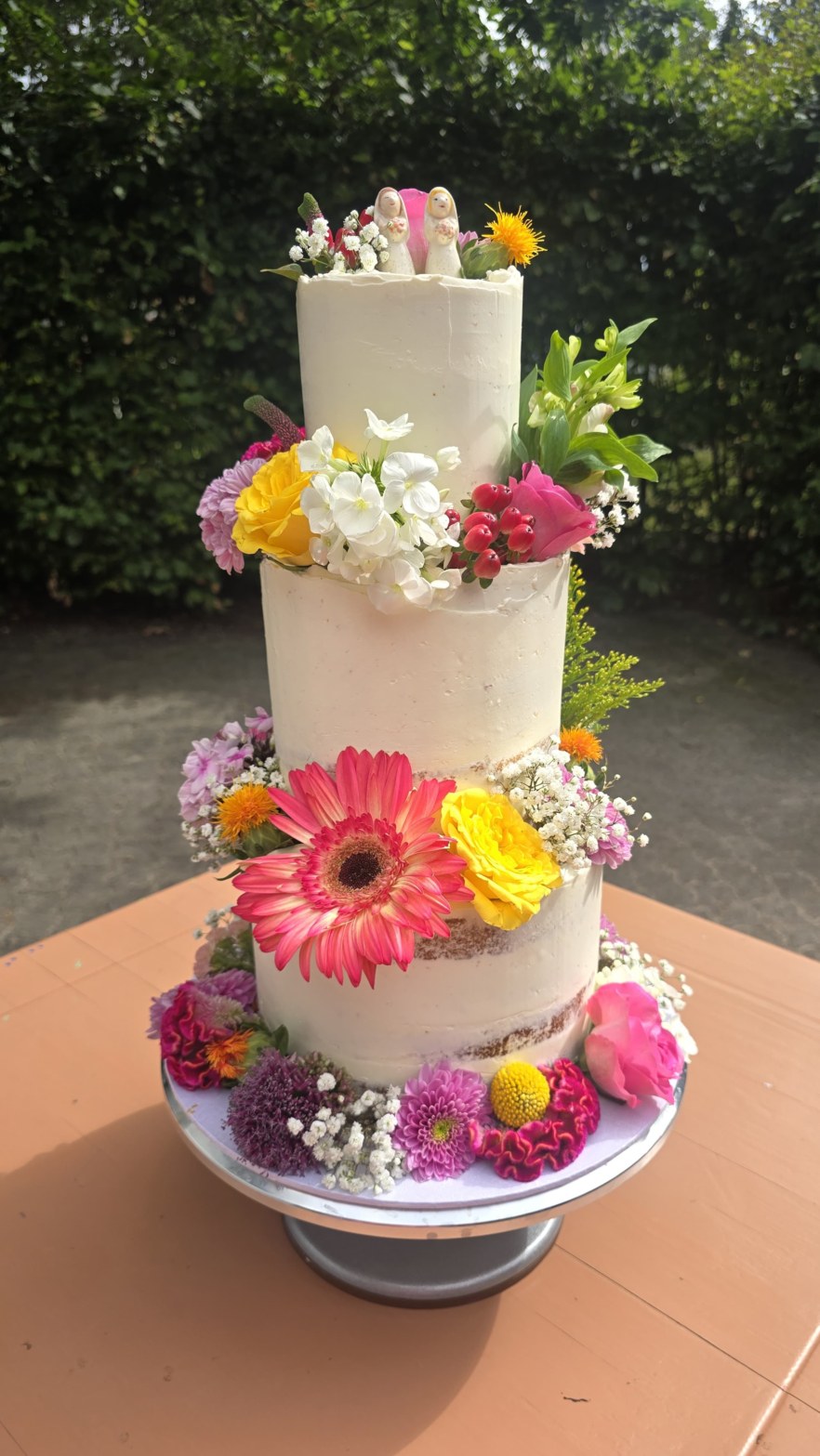 Klassieke bruidstaart van drie etages in witte botercrème met kleurrijke verse bloemen